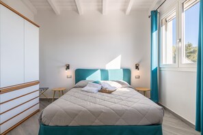 Ein Schlafzimmer mit einem Bett, zwei Nachttischen, einem Fenster mit Vorhängen und einem Kopfteil.
