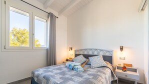 Een slaapkamer met een bed, twee nachtkastjes, een raam en uitzicht op bomen.