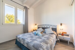 Ein Schlafzimmer mit einem Bett, zwei Nachttischen, einem Fenster und Blick auf Bäume.