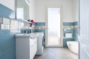 Une salle de bain équipée d’un lave-linge, d’un lavabo, d’un miroir et de toilettes.