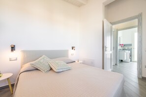 Une chambre à coucher avec un lit, des tables de chevet et une salle de bain visible à travers une porte ouverte.