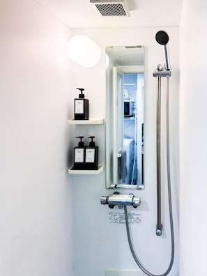 Et moderne badeværelse med bruser, spejl og to hylder med toiletartikler.