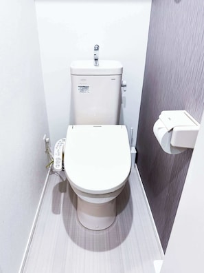 A compact, modern bathroom with a white toilet, a visible control panel, and a wall-mounted bidet.