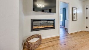 Un pasillo con chimenea, un televisor de pantalla plana montado sobre ella y una cesta de mimbre en el suelo.