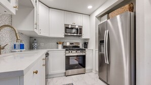 Una cocina moderna con armarios blancos, un refrigerador de acero inoxidable, un microondas y un horno.
