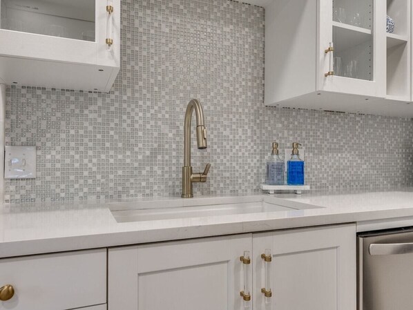 A kitchen with a white countertop, a gold faucet, and a tiled backsplash.