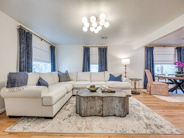 Una sala de estar con un sofá seccional, una mesa de centro y una zona de comedor con una mesa y sillas.
