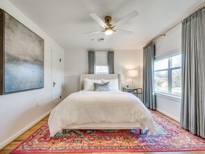 Un dormitorio con cama, ventilador de techo, ventana con cortinas y alfombra.