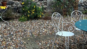 A stone wall, a metal chair, and a table with a potted plant. - Spacious Village House with Garden in Ginoles (Ginoles)