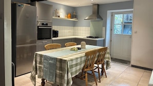 A modern kitchen with a dining table, chairs, and a refrigerator. - Spacious Village House with Garden in Ginoles (Ginoles)