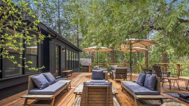 Een terras buiten met houten meubels, waaronder banken en stoelen, en een eethoek met tafels en parasols.