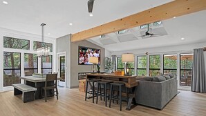 Een ruime woonkamer met houten plafond, grote ramen, een televisie en een bank.