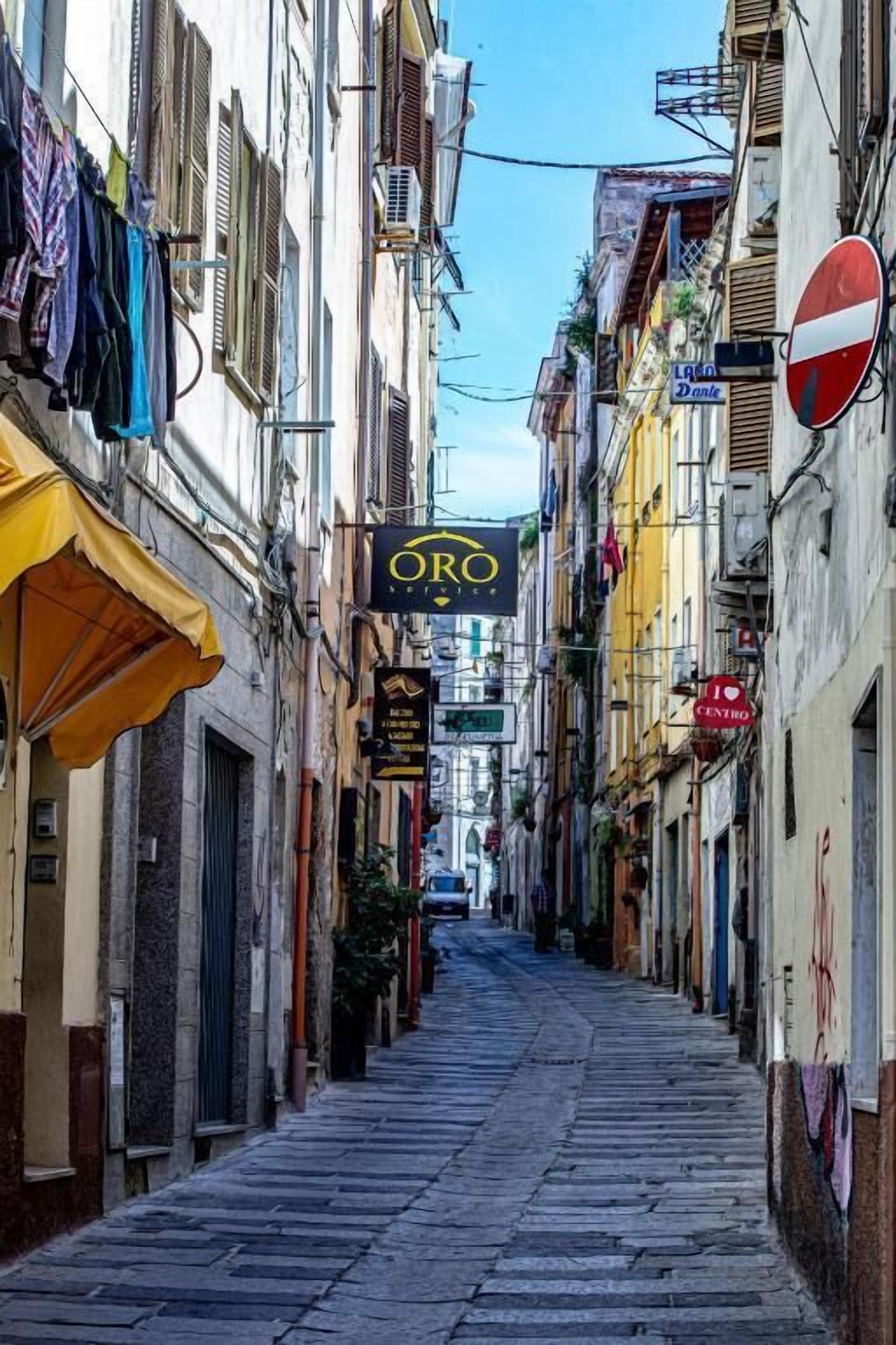 Una calle estrecha flanqueada por edificios, un letrero que dice 'Oro Hotel' y una señal de prohibido el paso.