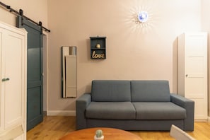 A living room with a grey sofa, a cabinet, a shelf with a 'love' sign, and a wall-mounted light fixture. - L'Accademia dei Sogni (Sassari)
