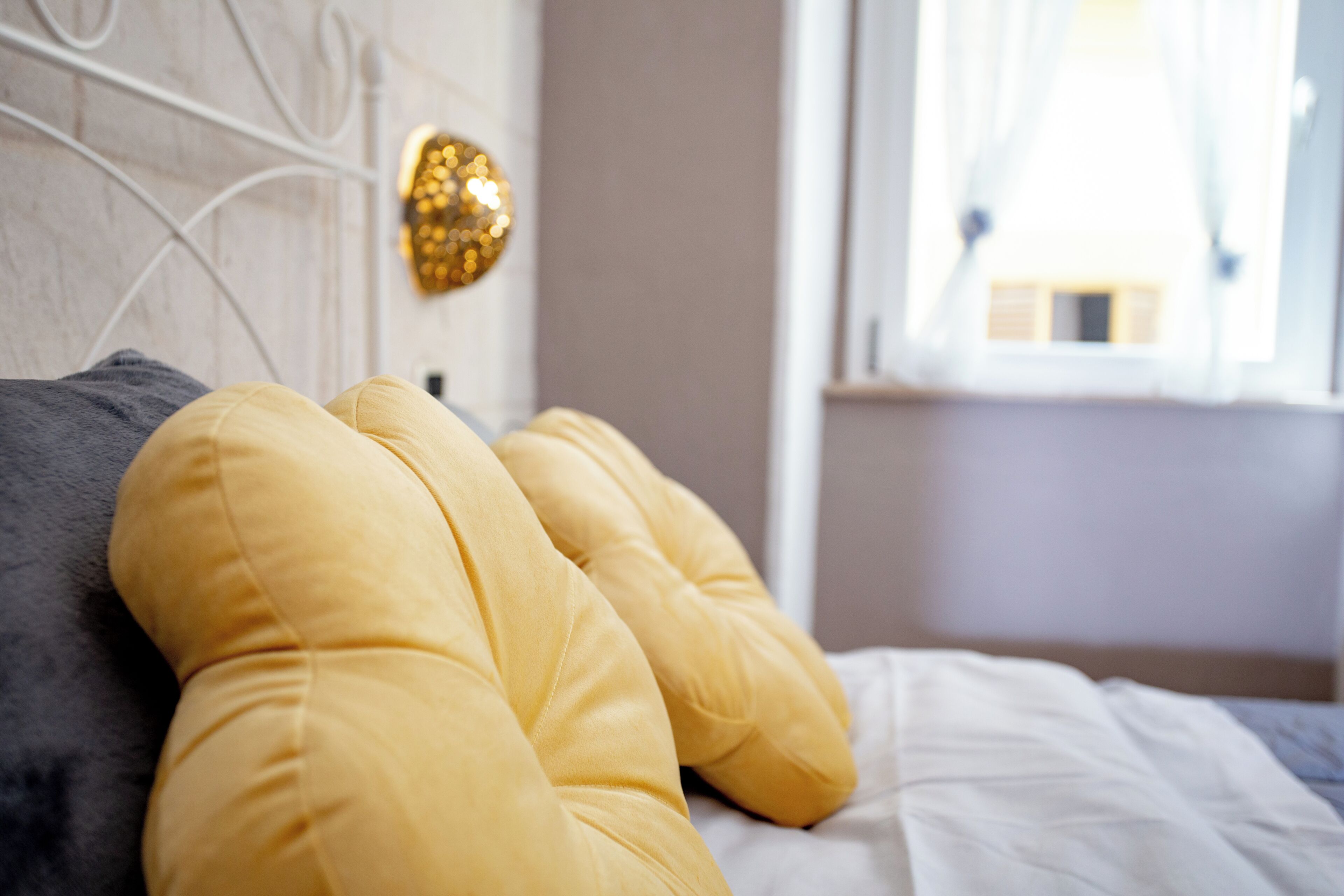 A bed with yellow and gray pillows, a white headboard, and a wall-mounted light fixture.