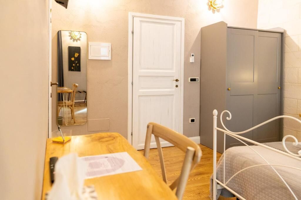A room with a wooden table, a white metal bed frame, a white door, and a grey wardrobe.