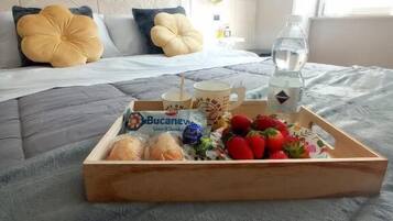 A neatly made breakfast tray with bread, strawberries, and a bottle of water on a bed with a white headboard and decorative pillows.