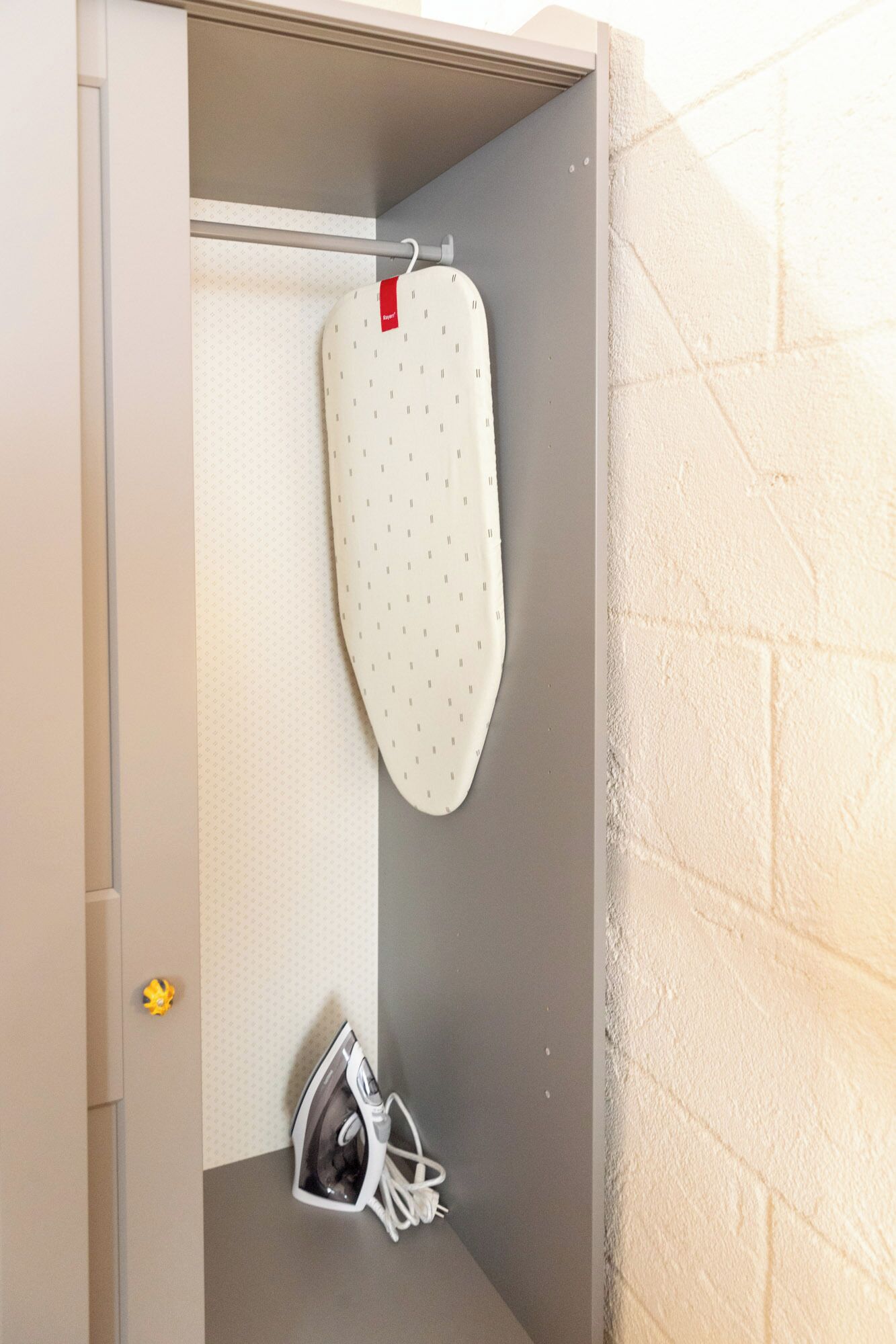 A small, enclosed space with a hanging ironing board, a pair of shoes, and a towel rack.