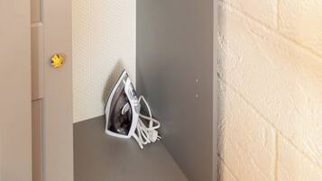 A small, enclosed space with a hanging ironing board, a pair of shoes, and a towel rack.