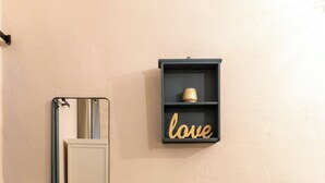 A room with a grey sofa, a wall-mounted mirror, and a shelf with a 'love' sign. - L'Accademia dei Sogni (Sassari)