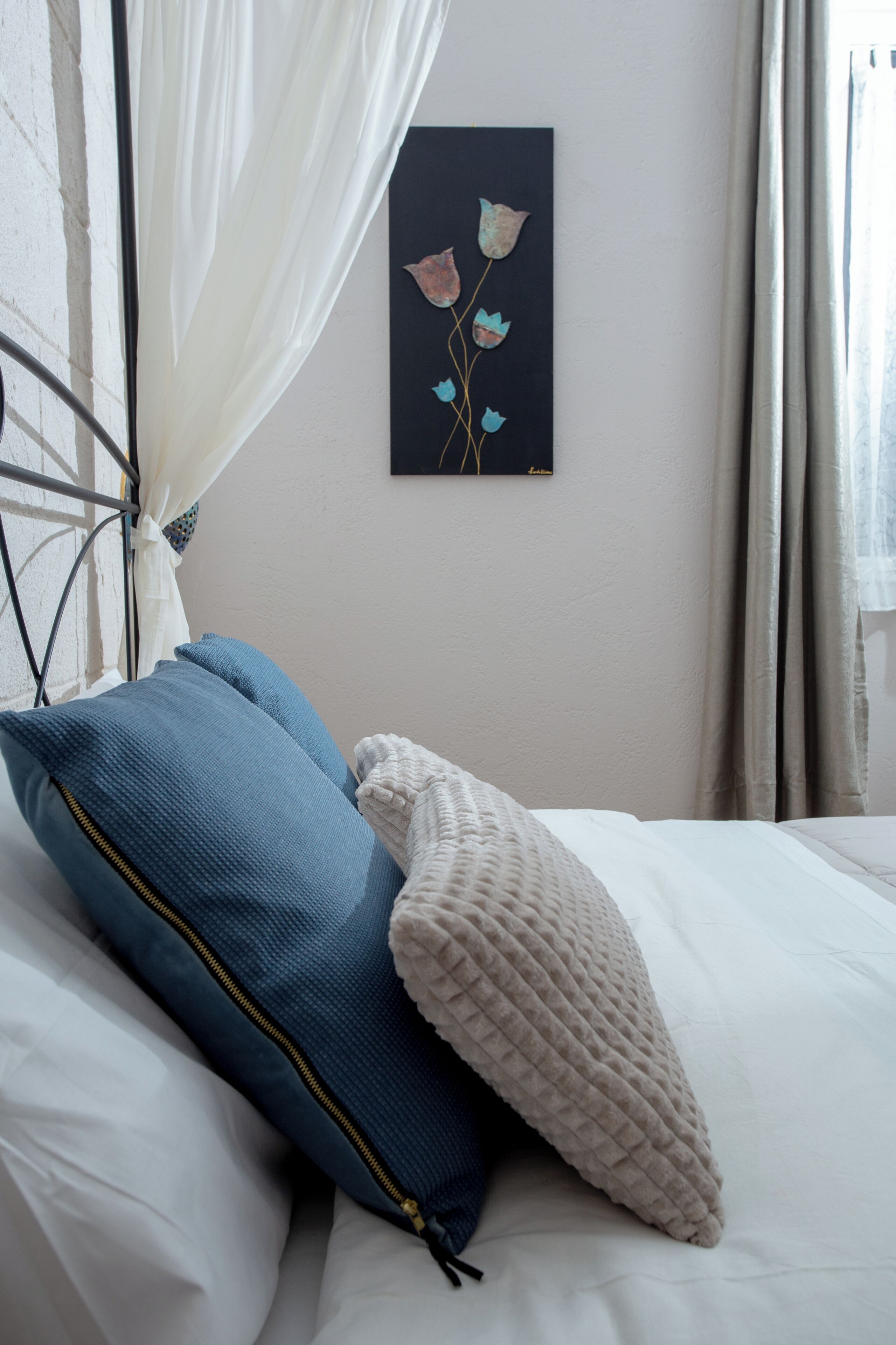 A bed with a white headboard, a blue pillow, a beige throw blanket, and a wall-mounted artwork of flowers.