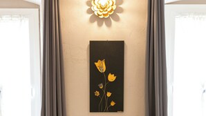 A room with a bench, a wall-mounted flower art piece, and a window with curtains. - L'Accademia dei Sogni (Sassari)
