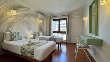 A hotel room with two beds, a desk, a mirror, and a view of the outside.