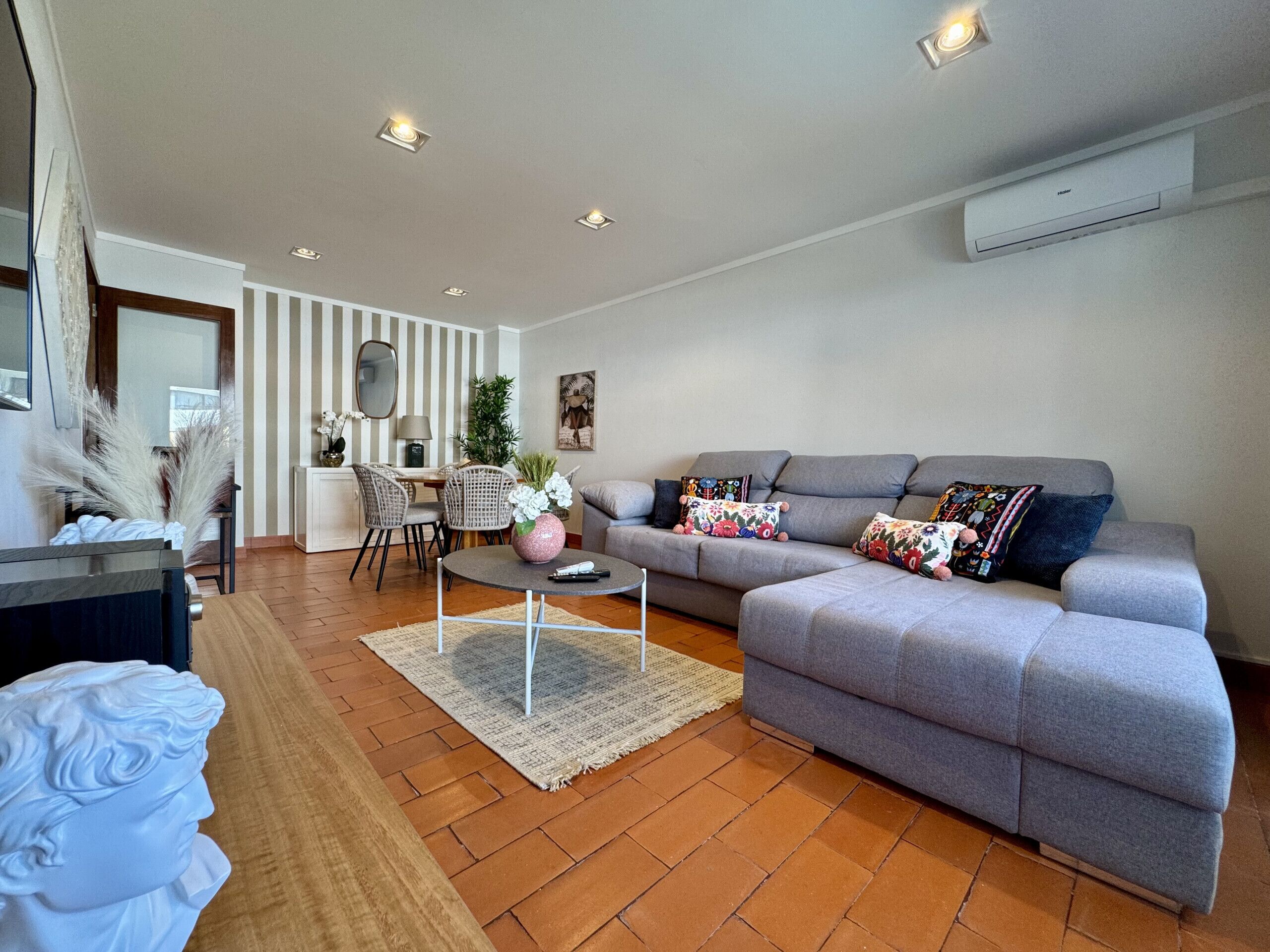 A modern living room with a grey sofa, a round coffee table, and a dining area with wicker chairs.
