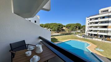 Un balcón con una mesa lista para el té, una piscina y vistas de edificios y zonas verdes circundantes.