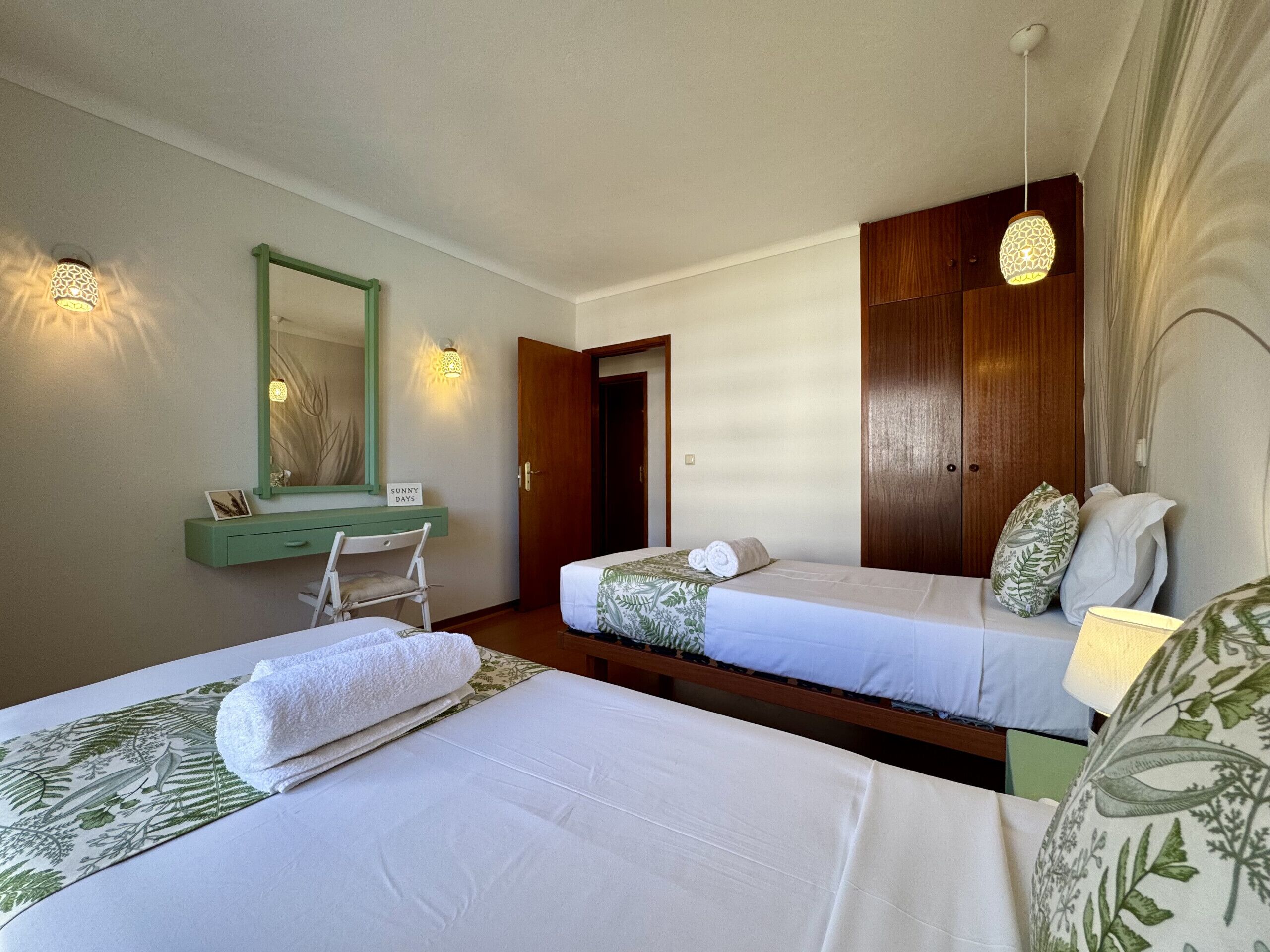 Habitación de hotel con dos camas, un tocador verde, un espejo y una puerta que da a otra habitación.