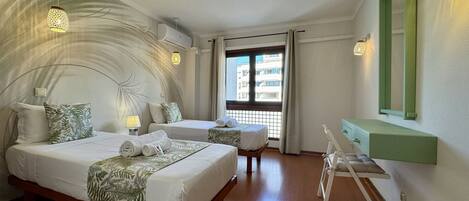 A hotel room with two beds, a desk, a mirror, and a view of the outside.