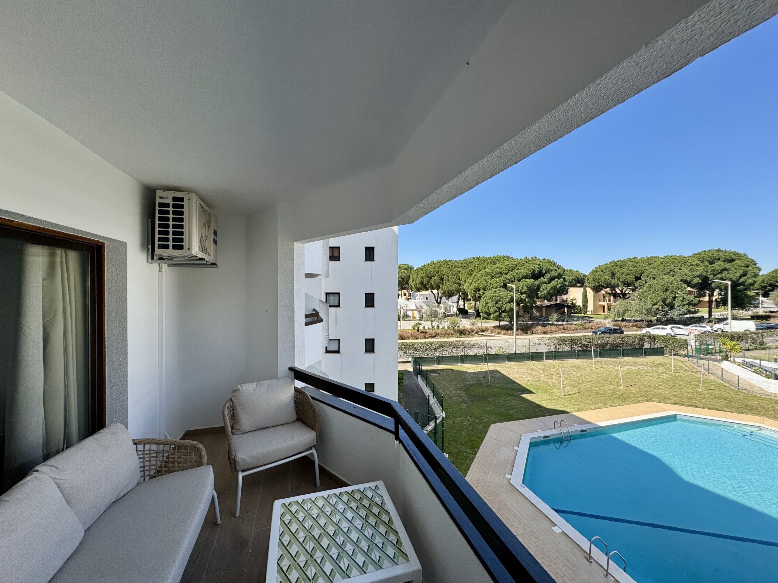 A balcony with a sofa, a chair, a pool, and a view of a residential area.