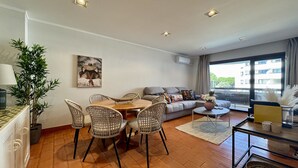 A living room with a dining area, a sofa, and a large window. - Vilamoura Charming 2 With Pool by Homing (Loulé)