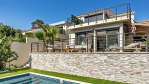 Ein modernes Haus mit Swimmingpool, einem Balkon mit Gartenmöbeln und einer Steinmauer.