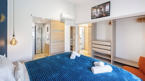 Ein modernes Hotelzimmer mit einem großen Bett, einem begehbaren Kleiderschrank und einem Badezimmer mit Duschkabine.