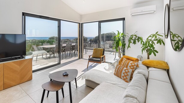 Ein modernes Wohnzimmer mit Fernseher, Sofa und Essbereich, mit großen Fenstern und einem Balkon.