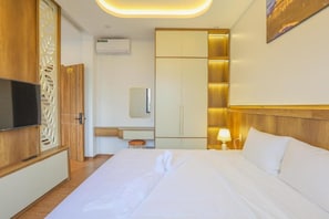 Habitación de hotel con cama, televisor, escritorio con silla, espejo y armario.