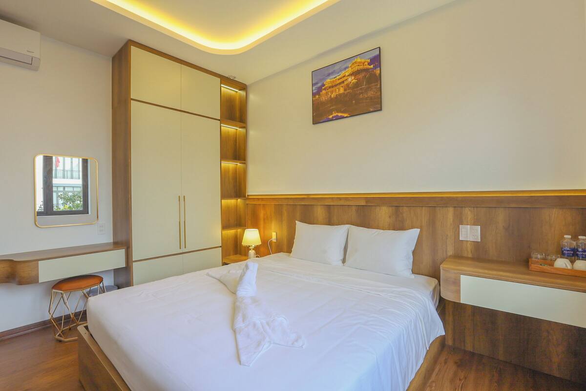A neatly made bed with a towel, a nightstand with a lamp, and a wooden headboard.