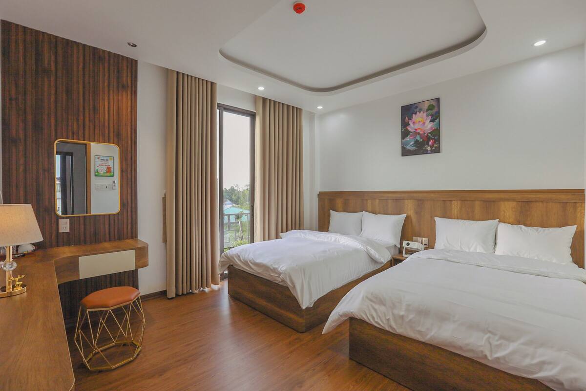 A hotel room with two beds, a desk with a chair, a mirror, and a window with curtains.