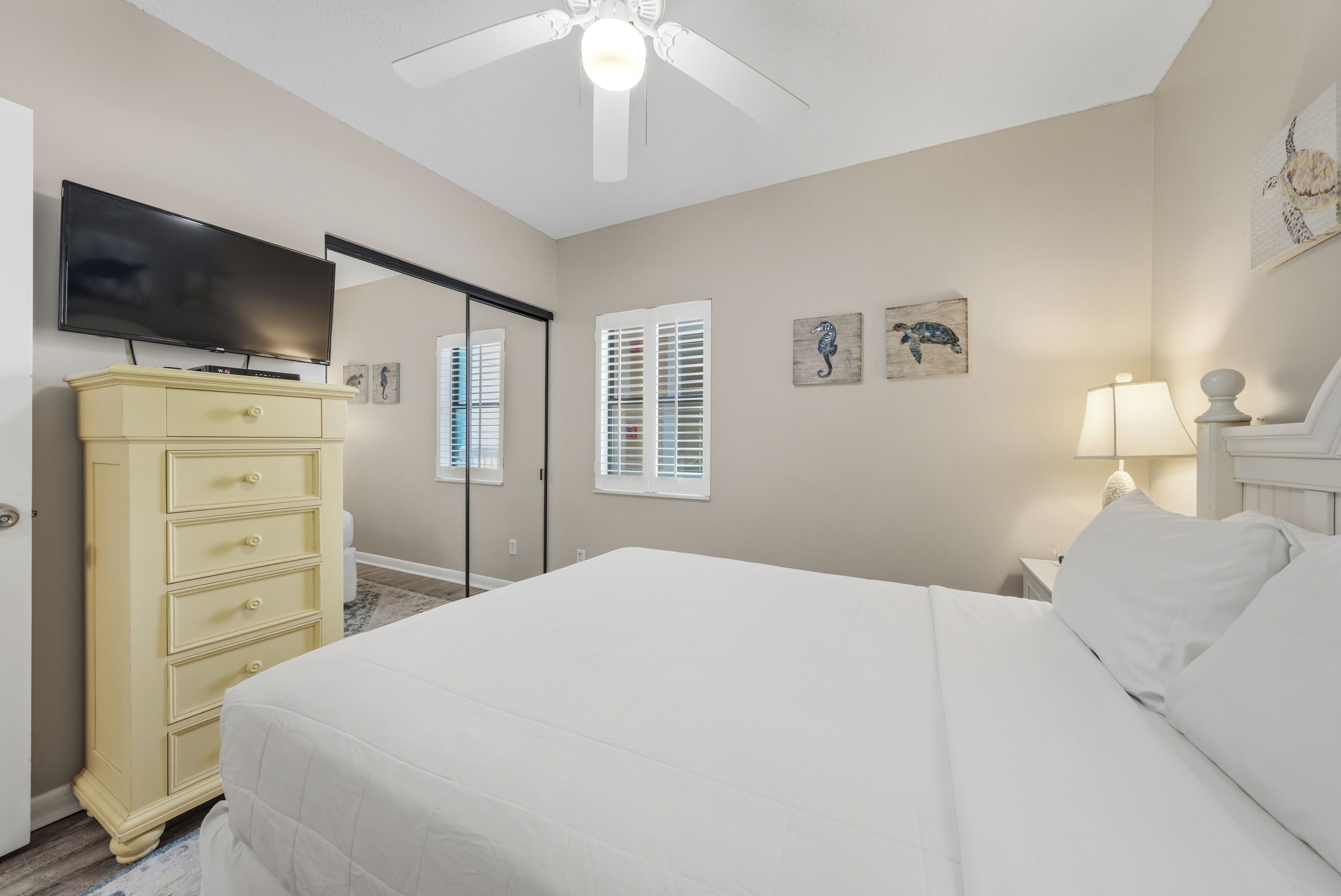 A bedroom with a bed, a dresser, a television, and a ceiling fan.
