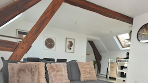 A modern loft with a grey sectional sofa, a wooden ceiling beam, a skylight, and a small round table.