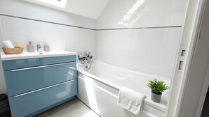 A modern bathroom with a bathtub, a blue vanity, a shower, and a skylight.