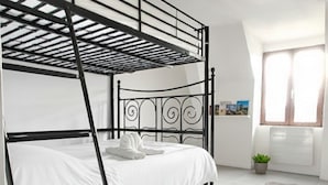 A bunk bed room with a ladder, white bedding, a small plant, and a window with curtains.