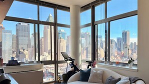 A modern living room with large windows, a sofa, a coffee table, and a desk with a laptop. - Luxury NYC Penthouse with Amazing Views (New York)