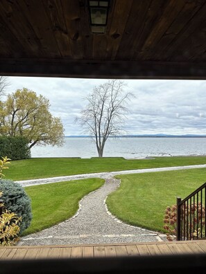 Blick von einer überdachten Veranda auf einen See, mit einem Kiesweg, der zum Wasser führt.