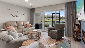 A modern living room with a sofa, armchair, coffee table, and a large TV screen. - Coastal Escape with Lake Views & Beach Days Just Minutes Away (Miramar Beach)