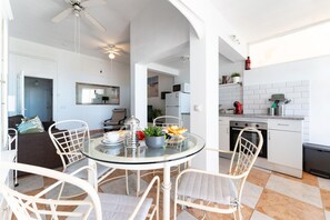 Una cocina moderna con armarios blancos, un comedor con mesa de vidrio y un ventilador de techo.