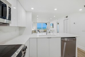 A modern kitchen with white cabinetry, a built-in microwave, and a dishwasher. - Renovated 3/2 Beach Condo Sand Castle I 205 Hot Tub Heated Pool (Indian Shores)