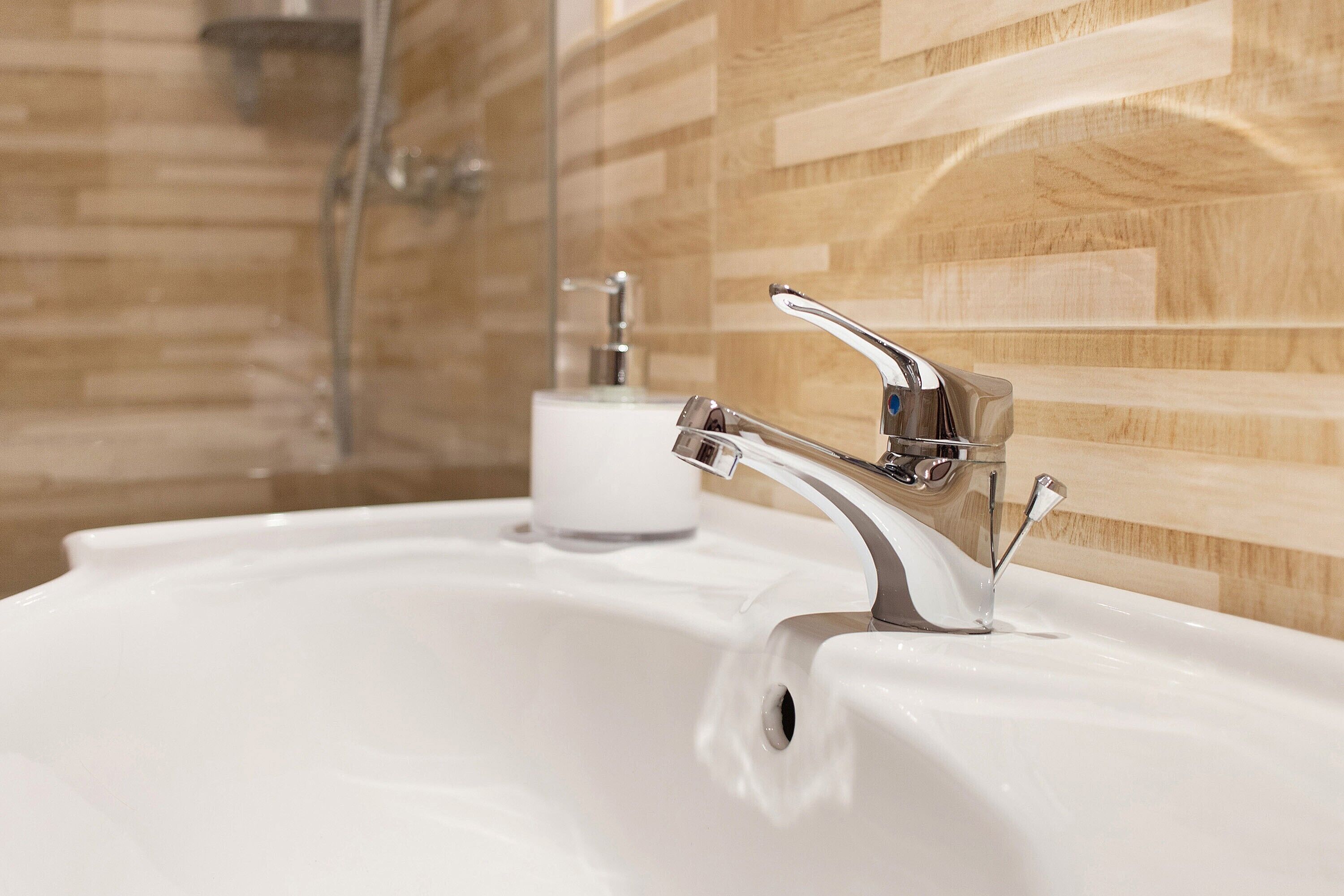 A bathroom with a white sink, chrome faucet, and wooden wall tiles.