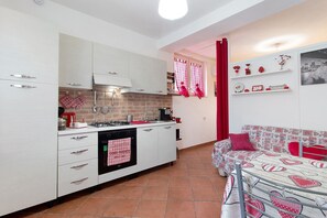 A compact kitchen with white cabinets, a gas stove, and a red towel hanging on the oven.